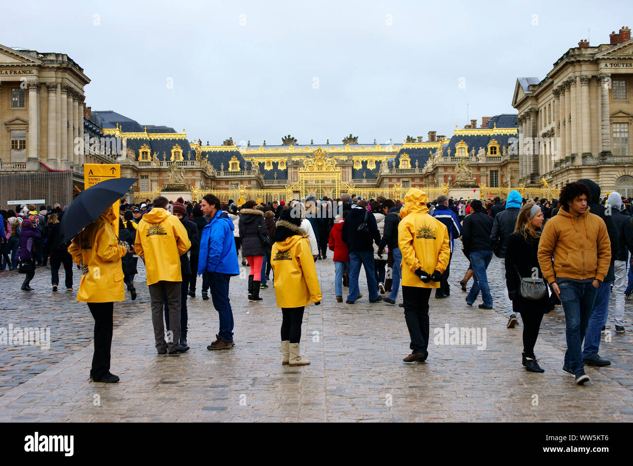 Staff and tourists standing in rainy weather at the entrance to the Palace of Versailles in Paris, Stock Photo