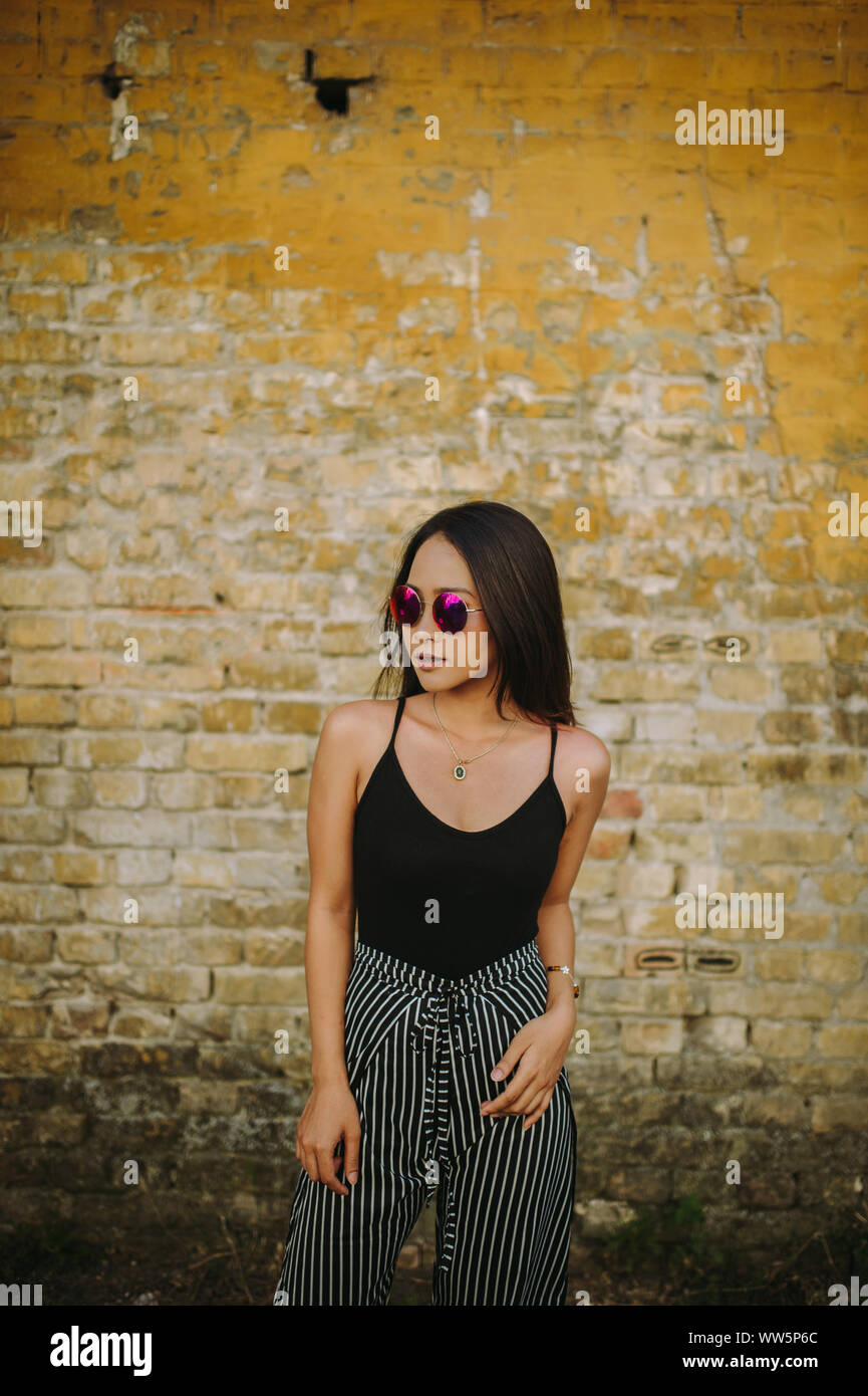 Portrait of a young woman standing in front of a brick wall Stock Photo ...