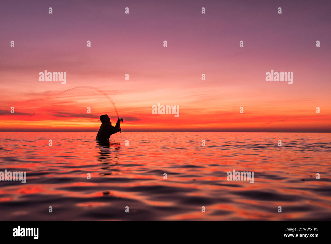 Angler fishing in the Baltic Sea at sundown standing in water. Stock Photo