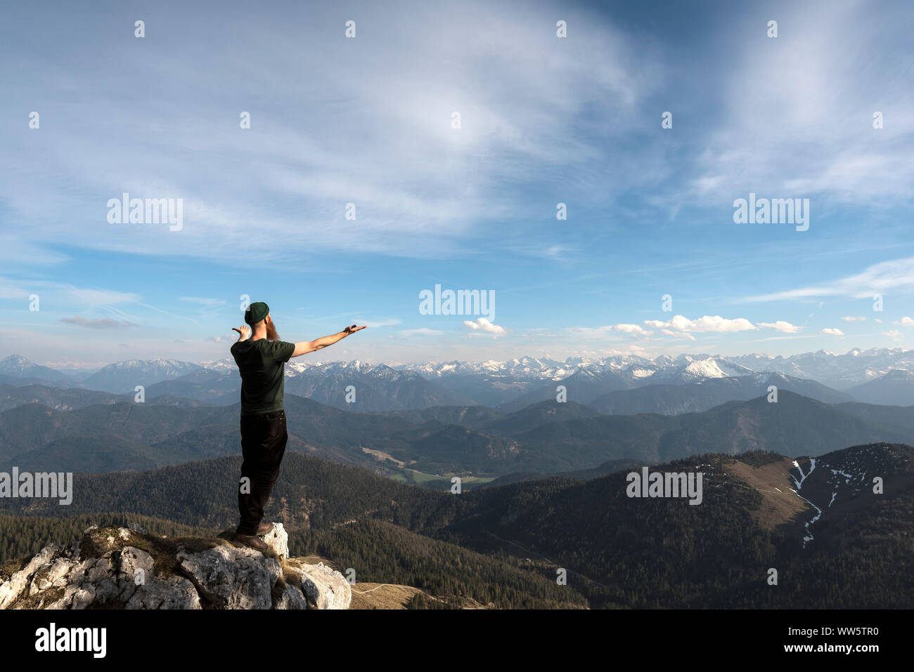 Mountaineer standing on boulder with outstretched arms in the direction of mountains Stock Photo