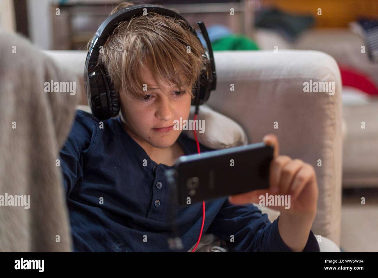 youngster at home on sofa watching his mobile phone with headset Stock Photo