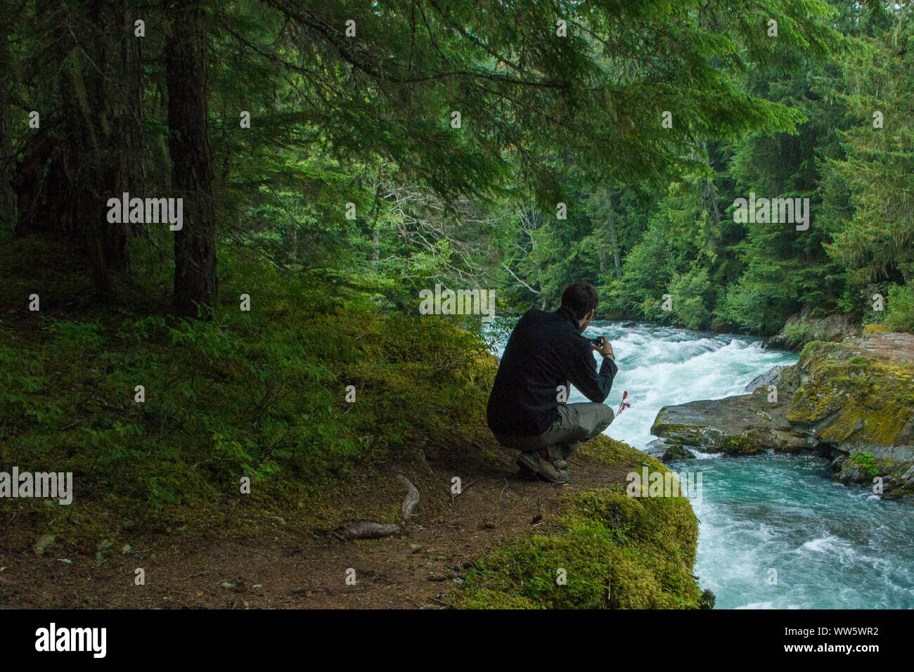 A man taking a photo of a tearing river in the Joffre Lakes Provincial Park, British Columbia, Canada Stock Photo