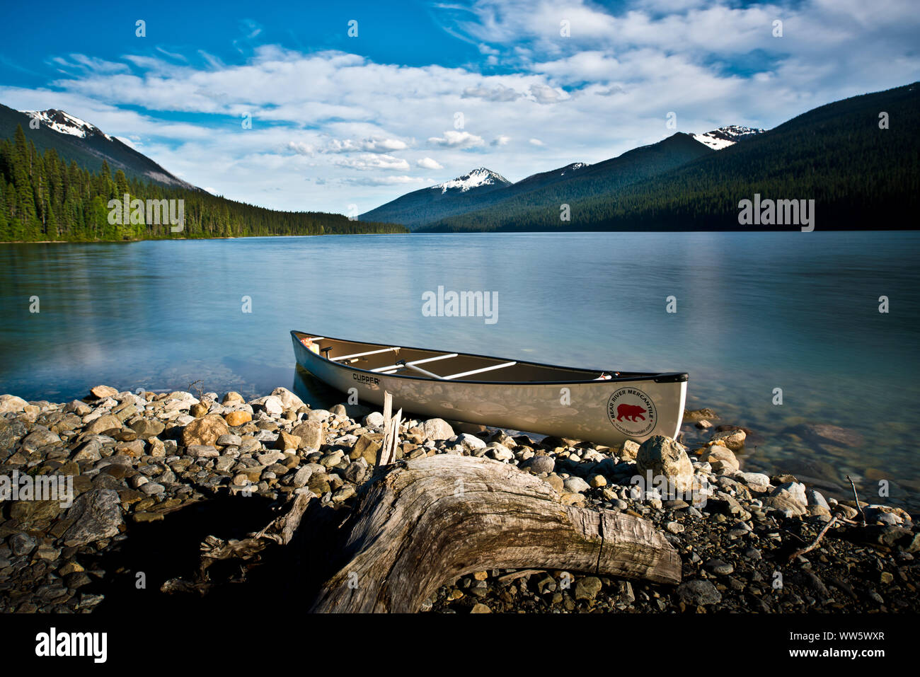 A canoe on the shore, in front of it a piece of wood decolorized by the sun, the water like glass, canoe trip in the Bowron Lake Provincial Park, Cariboo Mountains, Canada Stock Photo