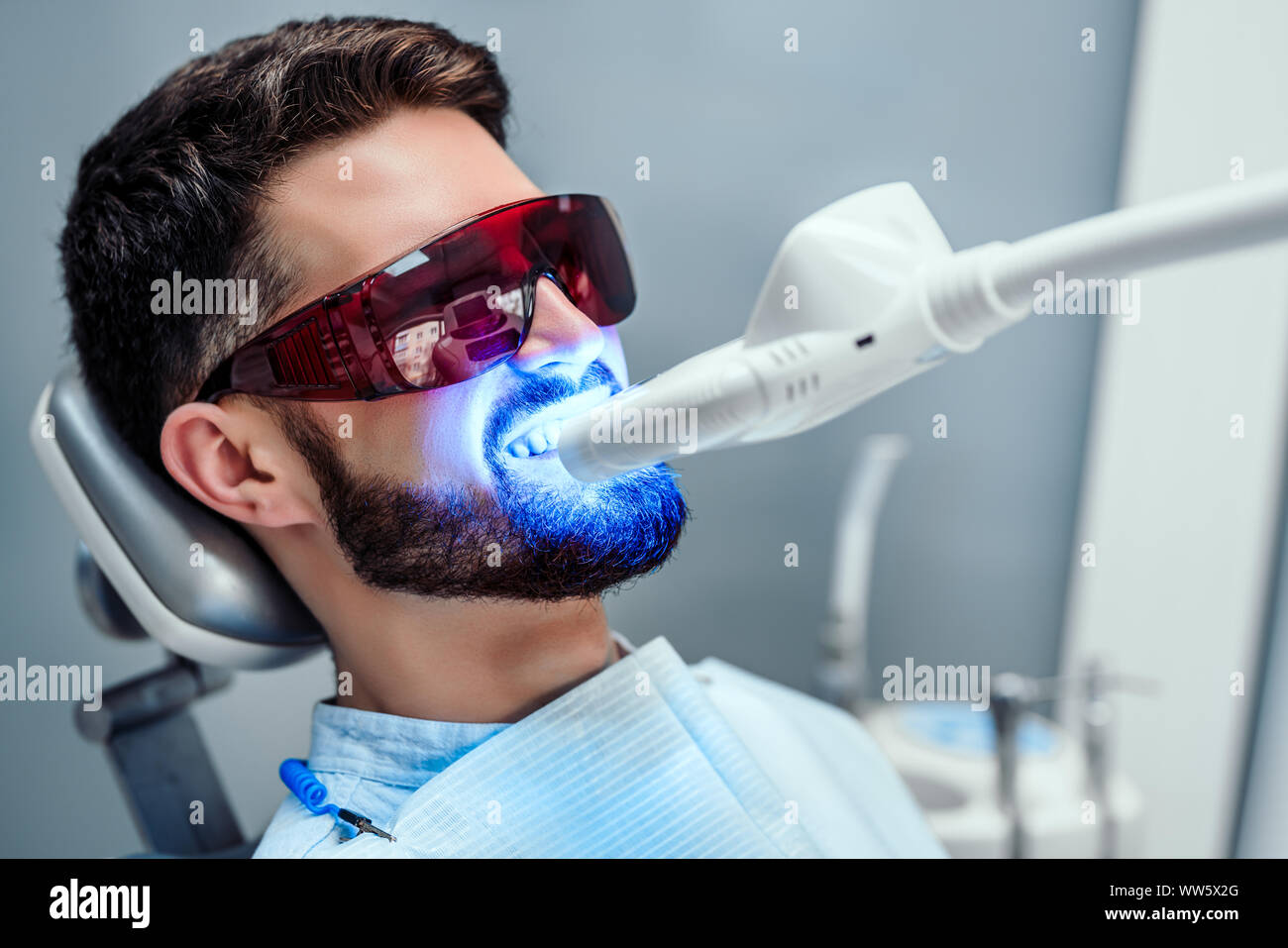 Close up view of man undergoing laser tooth whitening treatment to remove stains and discoloration. Stock Photo