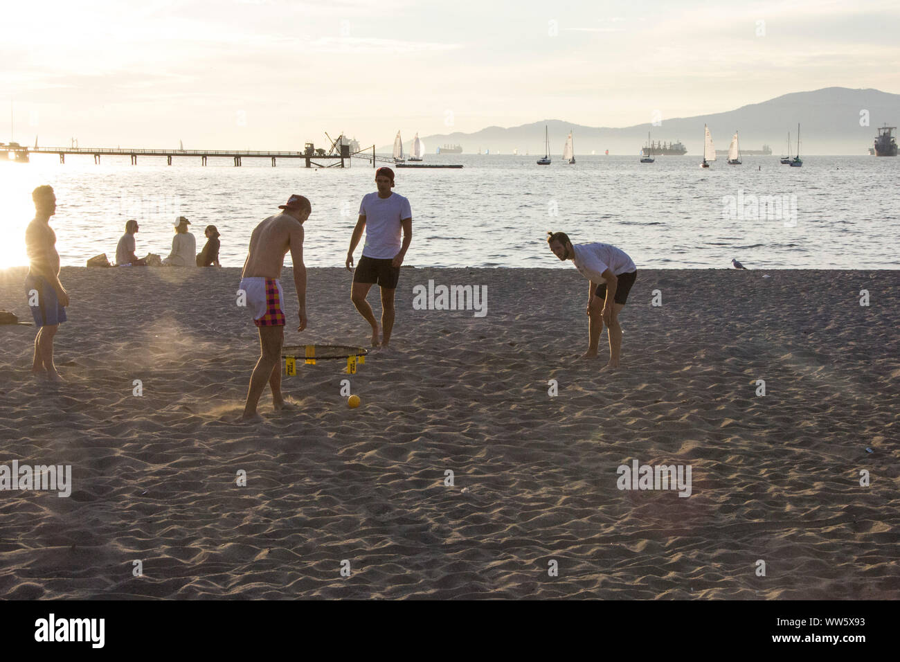Men playing with a ball on the beach, container ships in the horizon, English Bay, Vancouver Stock Photo