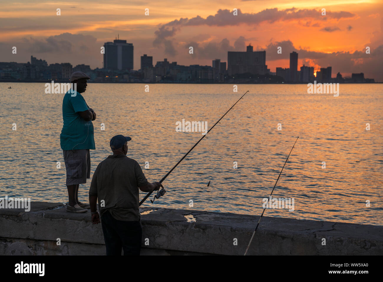 Angler as a silhouette at the Malecon in Havana, the city in the background, evening mood, orange and violet colours Stock Photo