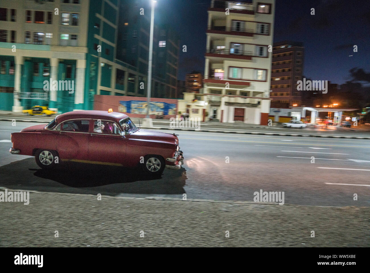 dark red vintage car driving through the night in Havana, Cuba Stock Photo