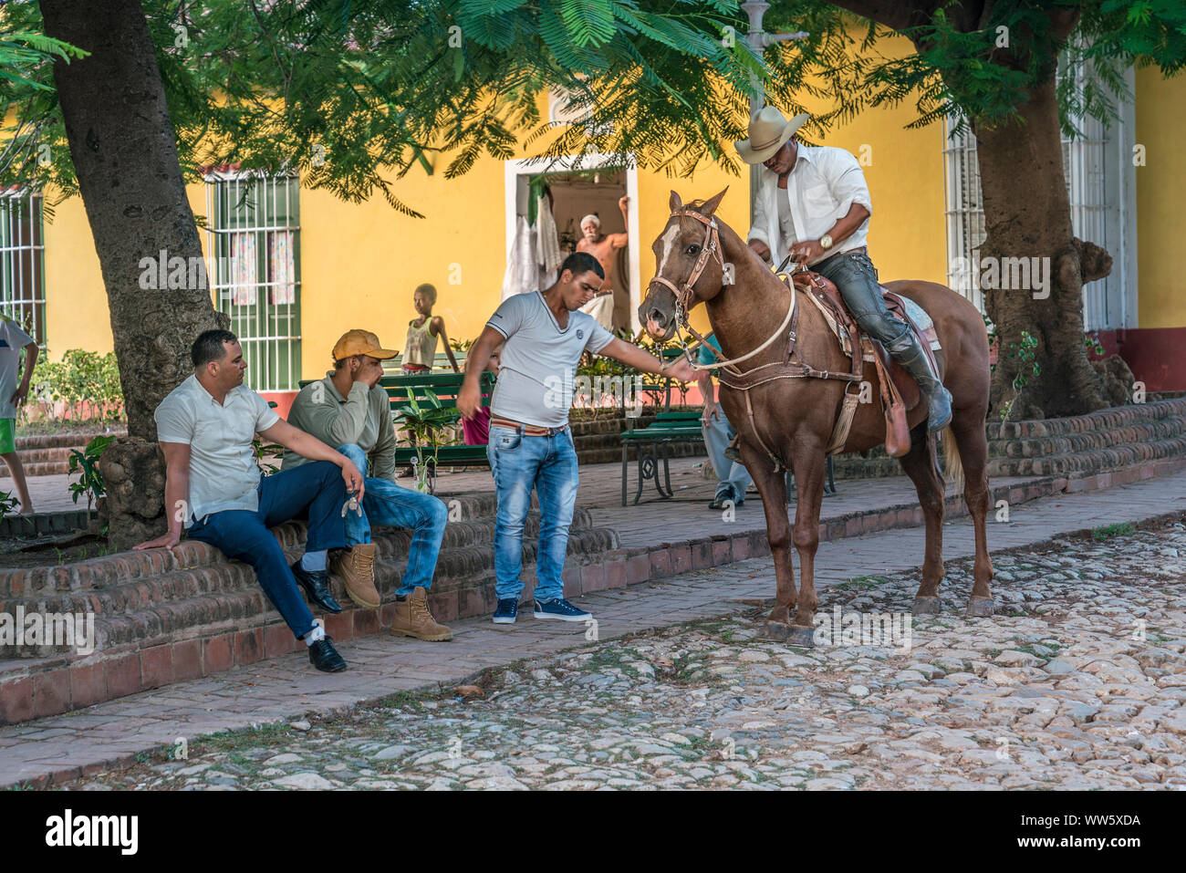 Men sitting on a square in the shadow of a tree, rider and horse Stock Photo