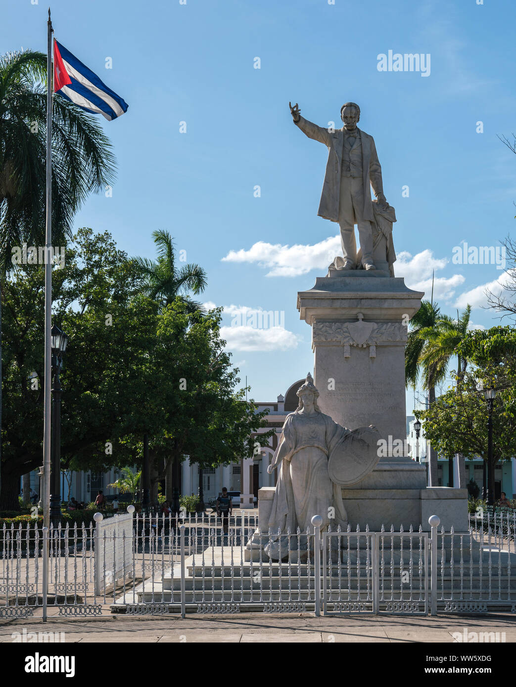 Statue of JosÃ© MartÃ, Cuban poet and author, in JosÃ© MartÃ Park, Cienfuegos, Cuba, beside him blowing the flag of Cuba Stock Photo