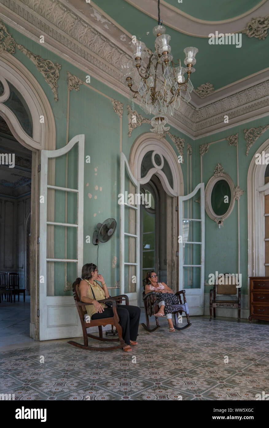 Palacio Ferrer was built in 1917-18 by Spanish squire JosÃ© Ferrer, Today the building is open for the public, The image showing a room of the Palacio with interior arrangement and two 'museum attendants' in the rocking chair, Cienfuegos, Cuba Stock Photo