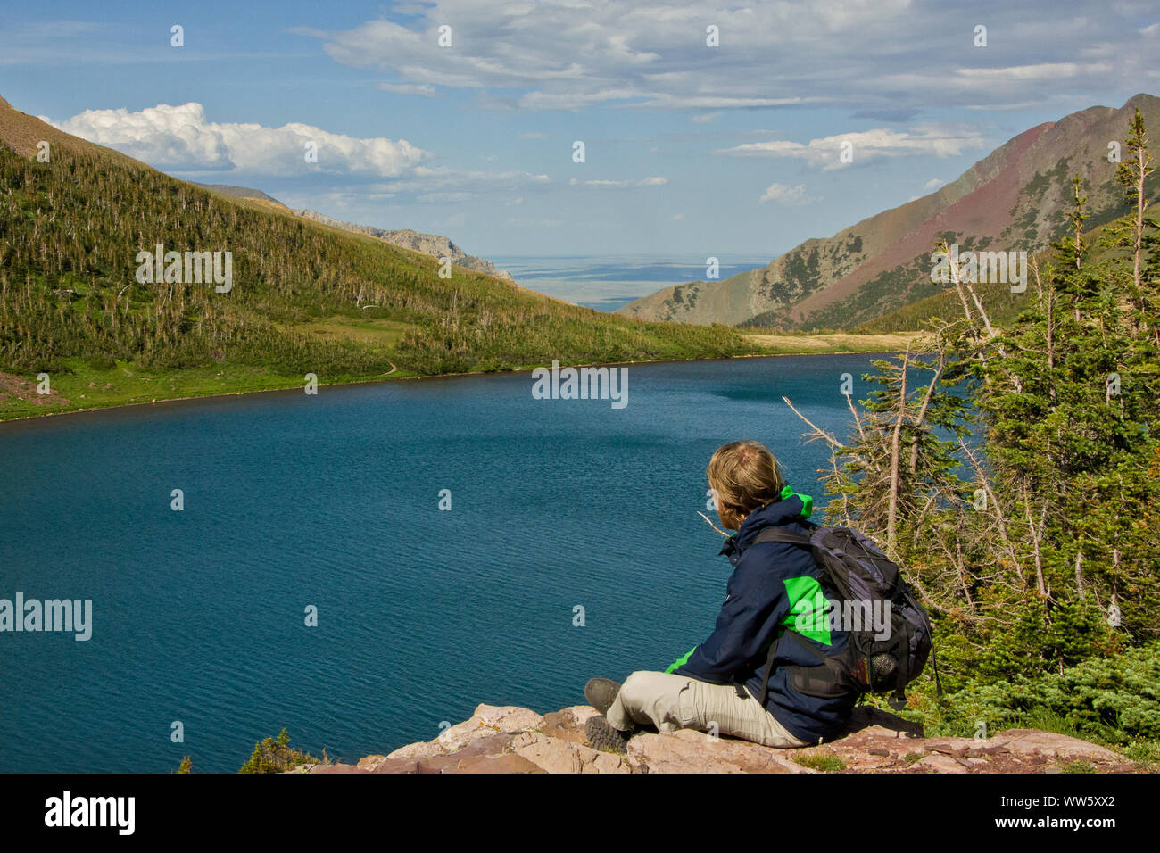 Young man sitting on a rock and looking over a mountain lake in the valley, Rocky Mountains, Alberta, Canada Stock Photo