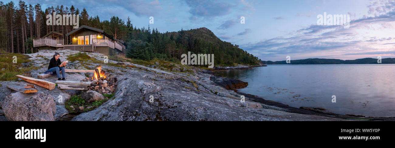 panoramic view woman reading near campfire in norway, fosnes,trondelag Stock Photo