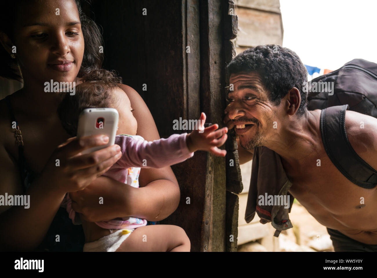 Three generations, young woman sitting with her baby and using her mobile phone, the grandfather making fun with the child on her arm Stock Photo