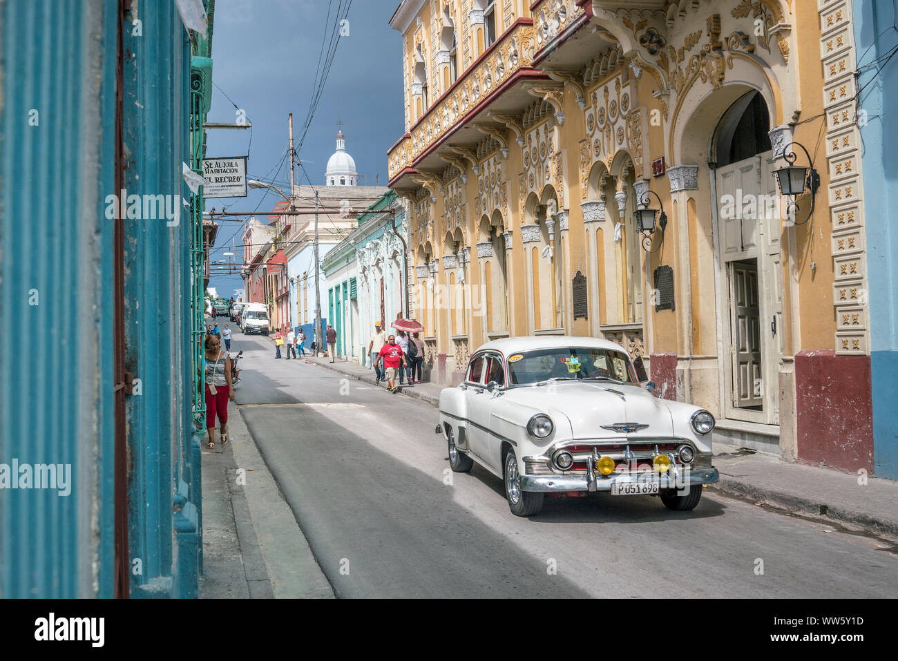 A white vintage car driving through a street in Santiago de Cuba Stock Photo