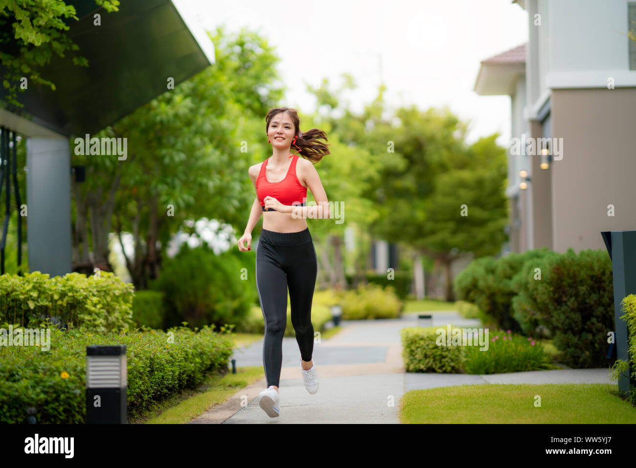 Jogging woman running in village in sunshine on beautiful summer day. Sport fitness model Asian ethnicity training outdoor for marathon. Stock Photo