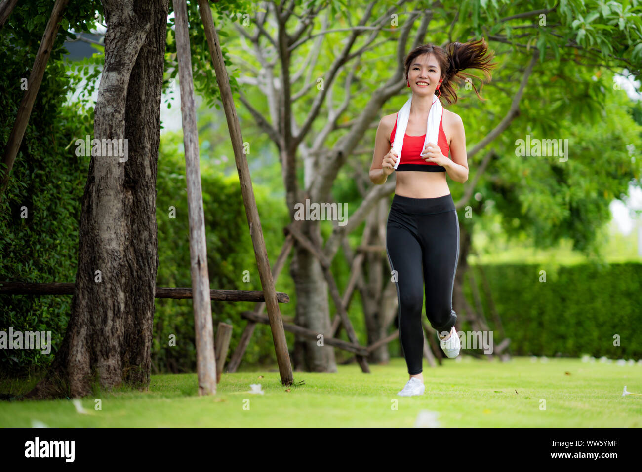 Jogging woman running in park in sunshine on beautiful summer day. Sport fitness model Asian ethnicity training outdoor for marathon. Stock Photo