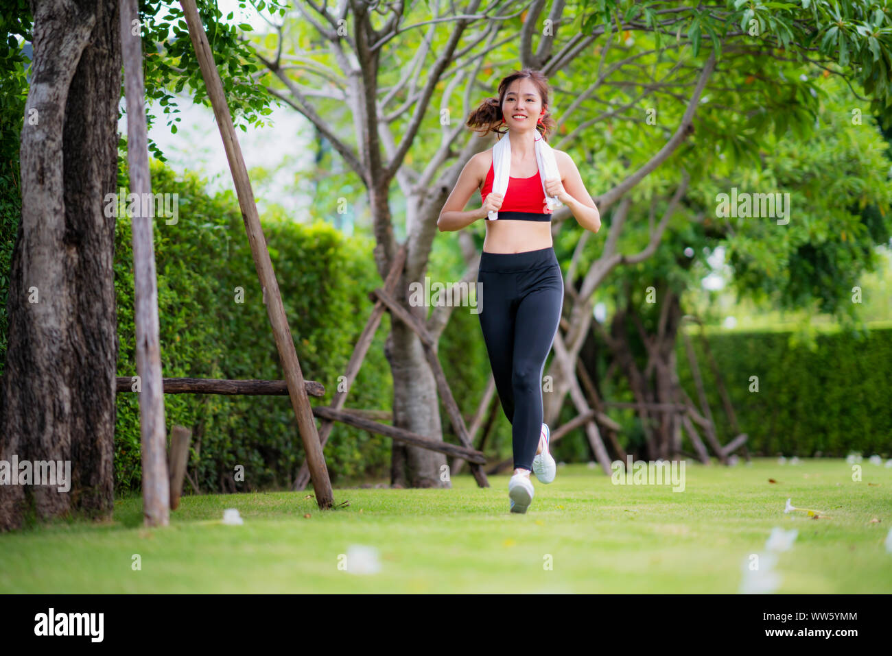 Jogging woman running in park in sunshine on beautiful summer day. Sport fitness model Asian ethnicity training outdoor for marathon. Stock Photo