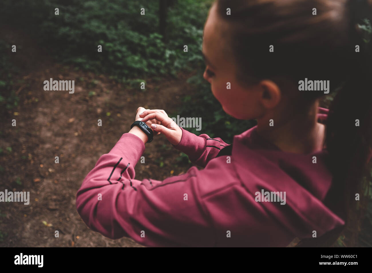 Cropped top view of a sporty girl setting fitness bracelet on training in the forest. Smart watch on a sporting girl wrist. Smart watch health, heart Stock Photo