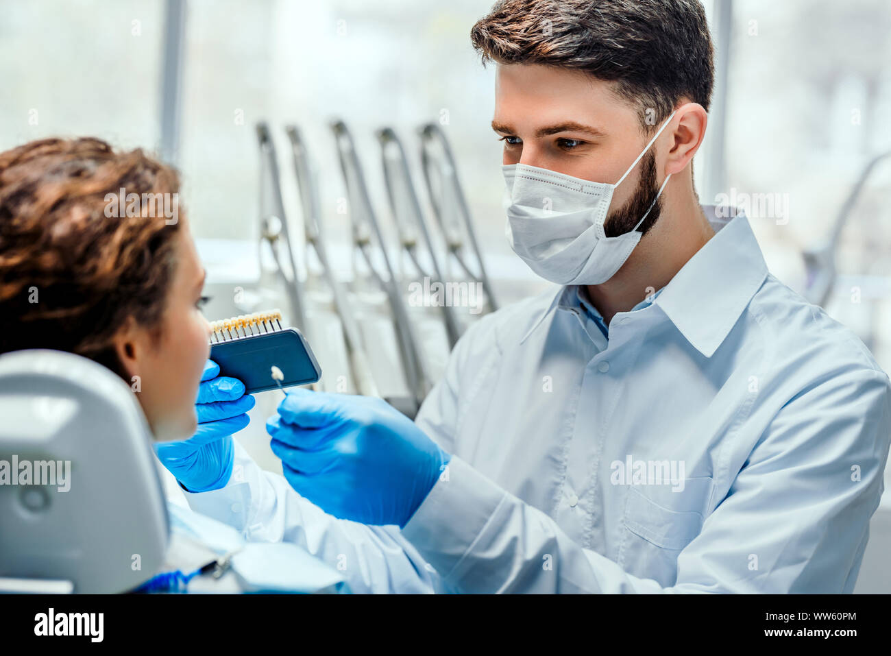 Dentist selecting patient's teeth color with palette in clinic. Side view. Stock Photo
