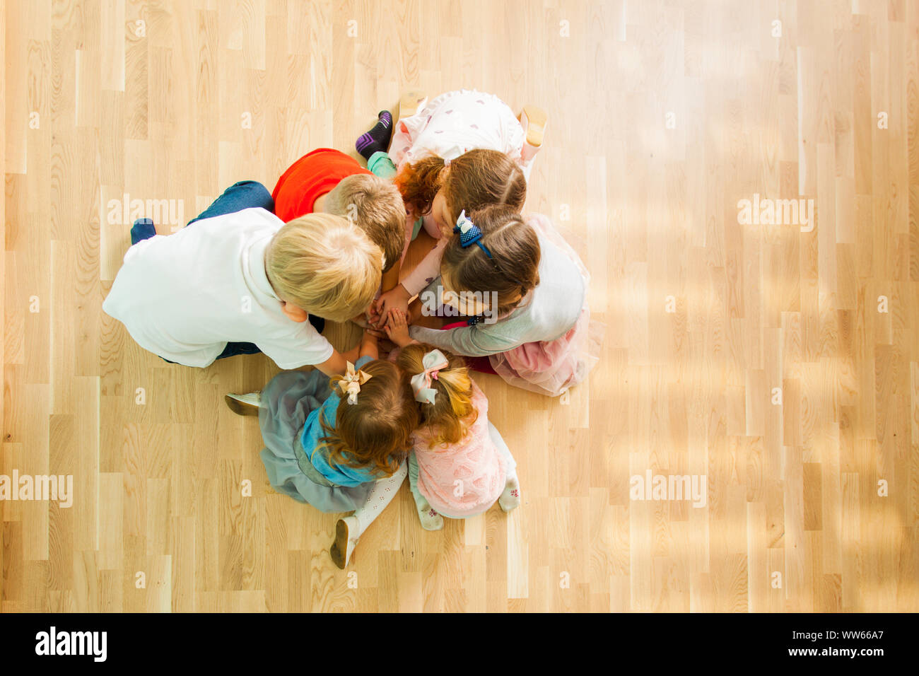 Top View Of Six Kids Closely Sitting Together On A Wooden Floor