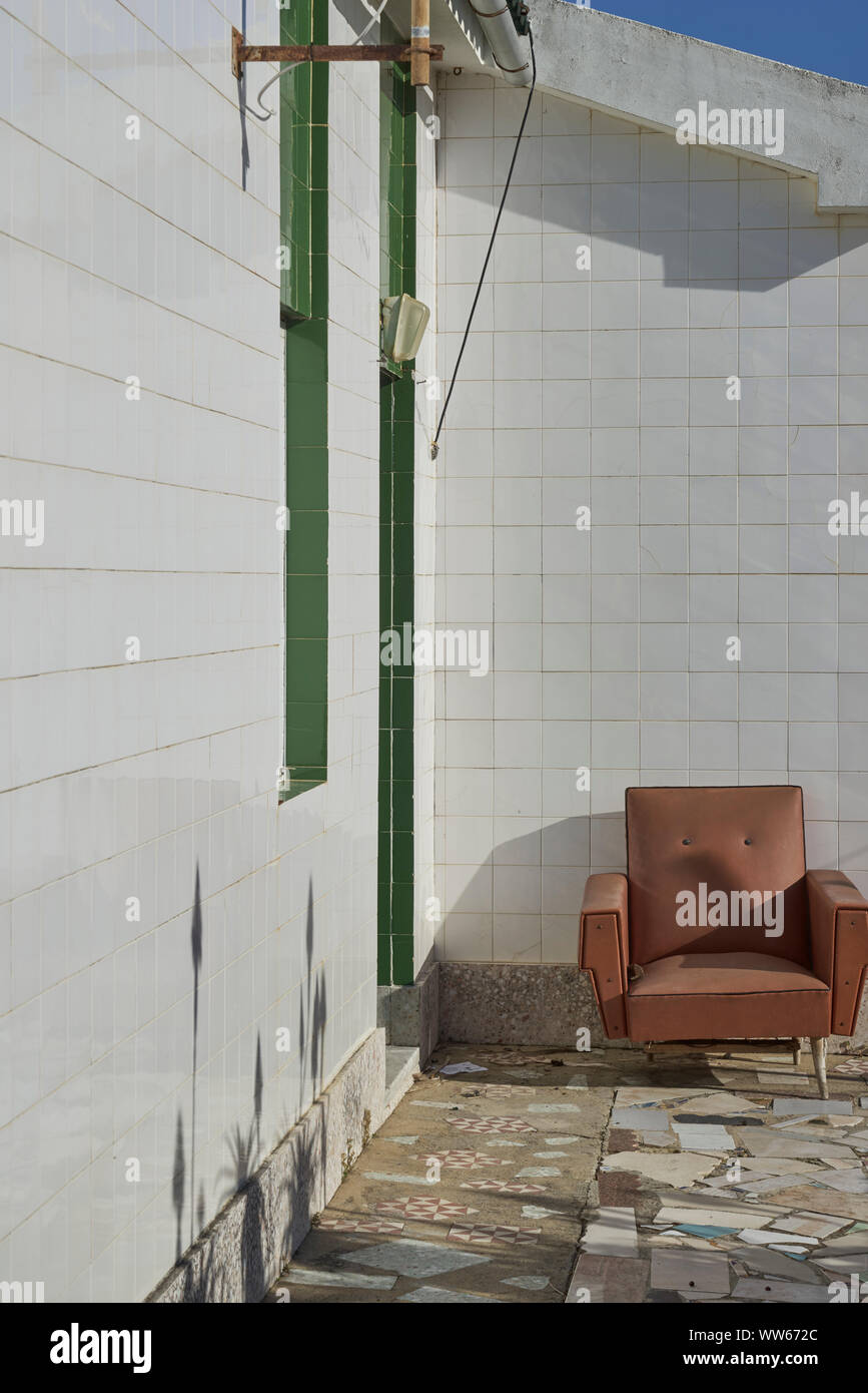 Old brown armchair on terrace with coloured tiles Stock Photo
