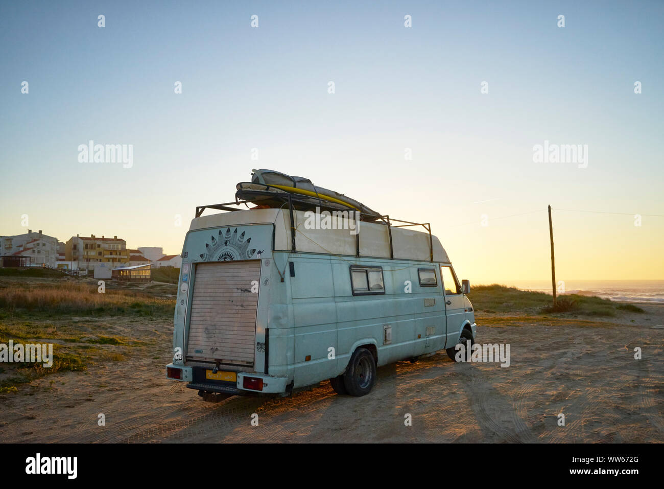 Old camper on the beach, surfboard on the roof Stock Photo