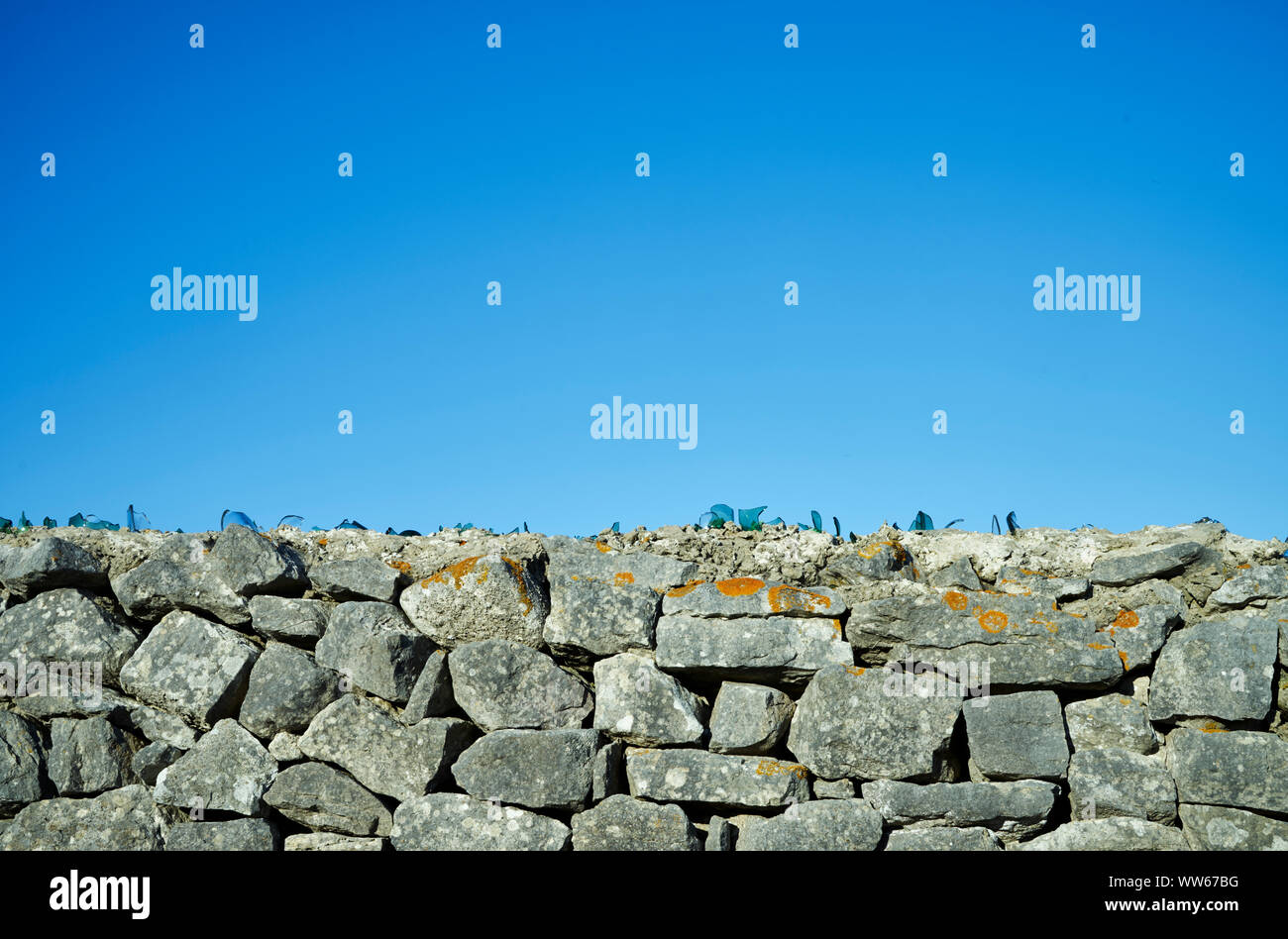 Glass shards on a stone wall in front of blue sky Stock Photo