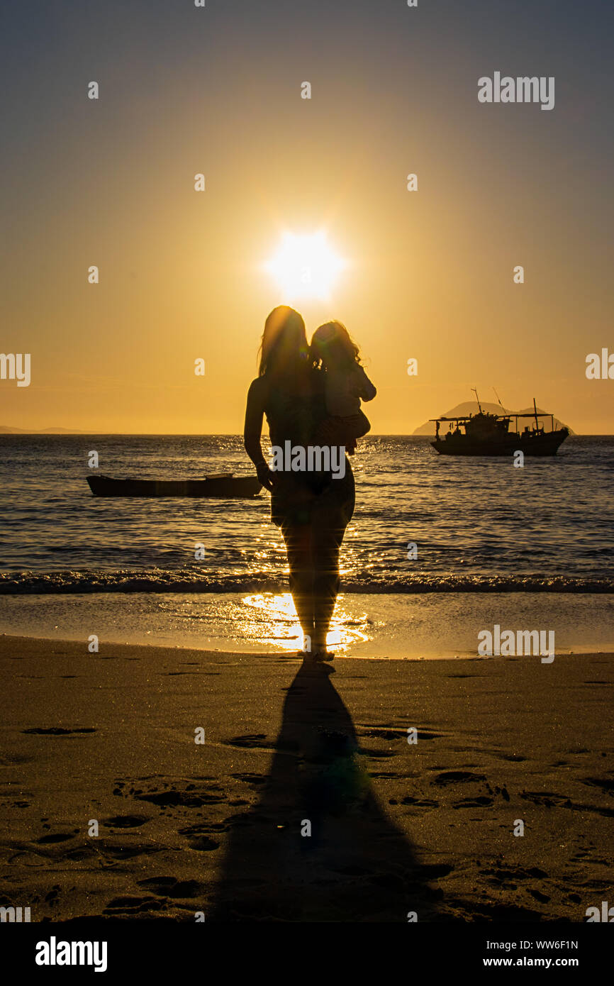 Silhouette of a woman standing on beach carrying her daughter, Brazil Stock Photo