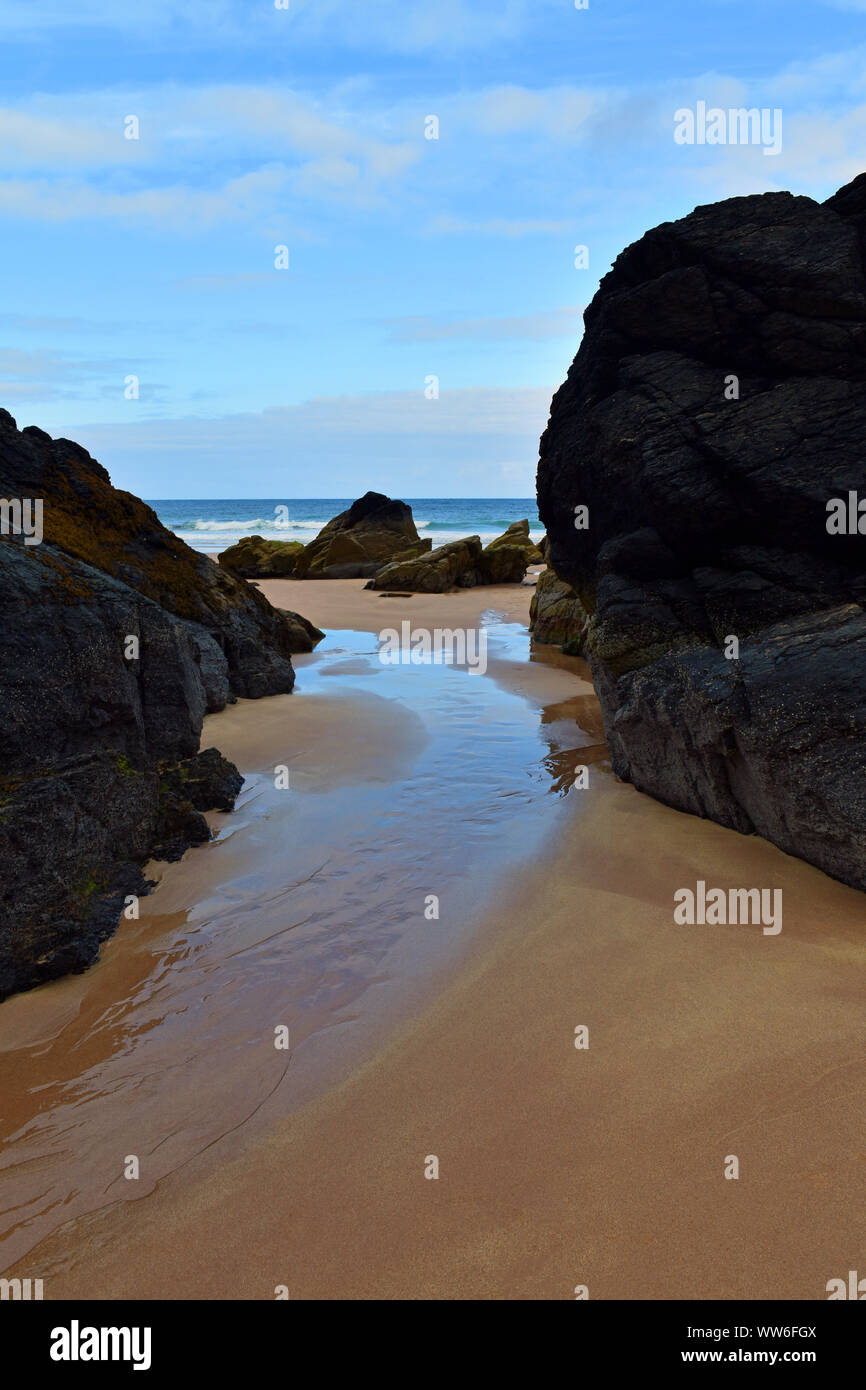 Simple seascape with pristine sand, large rocks and pathway to ocean with blue skies, taken at Durness, Scottish Highlands, North Coast 500 route Stock Photo