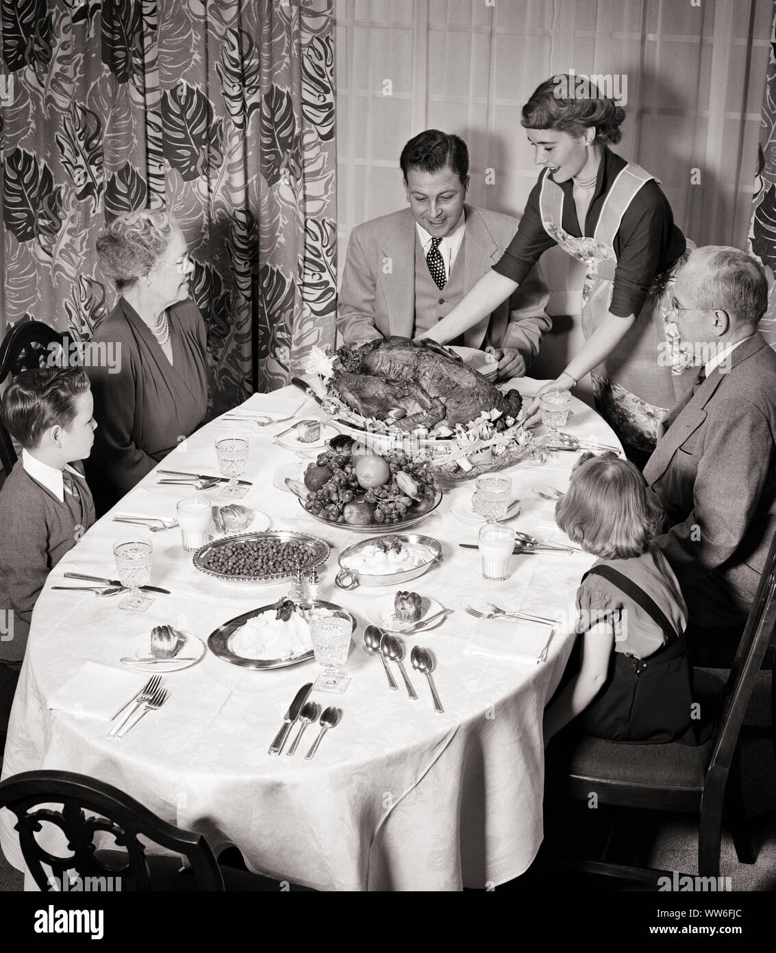 1950s THREE GENERATION FAMILY SITTING AROUND DINING ROOM TABLE AS MOTHER SERVES THANKSGIVING ROAST TURKEY - d2830 HAR001 HARS OLD TIME BUSY NOSTALGIA OLD FASHION JUVENILE TEAMWORK GRANDFATHER GRANDPARENTS PLEASED FAMILIES JOY LIFESTYLE SATISFACTION CELEBRATION FEMALES MARRIED GRANDPARENT SPOUSE HUSBANDS HEALTHINESS HOME LIFE 6 COPY SPACE HALF-LENGTH LADIES PERSONS CARING MALES SIX SPIRITUALITY SENIOR MAN AMERICANA SENIOR ADULT B&W PARTNER SENIOR WOMAN FREEDOM SUCCESS WIDE ANGLE HAPPINESS CHEERFUL STRENGTH EXCITEMENT PRIDE AS THREE GENERATION AUTHORITY GRANDMOTHERS SMILES THANKFUL GRANDFATHERS Stock Photo