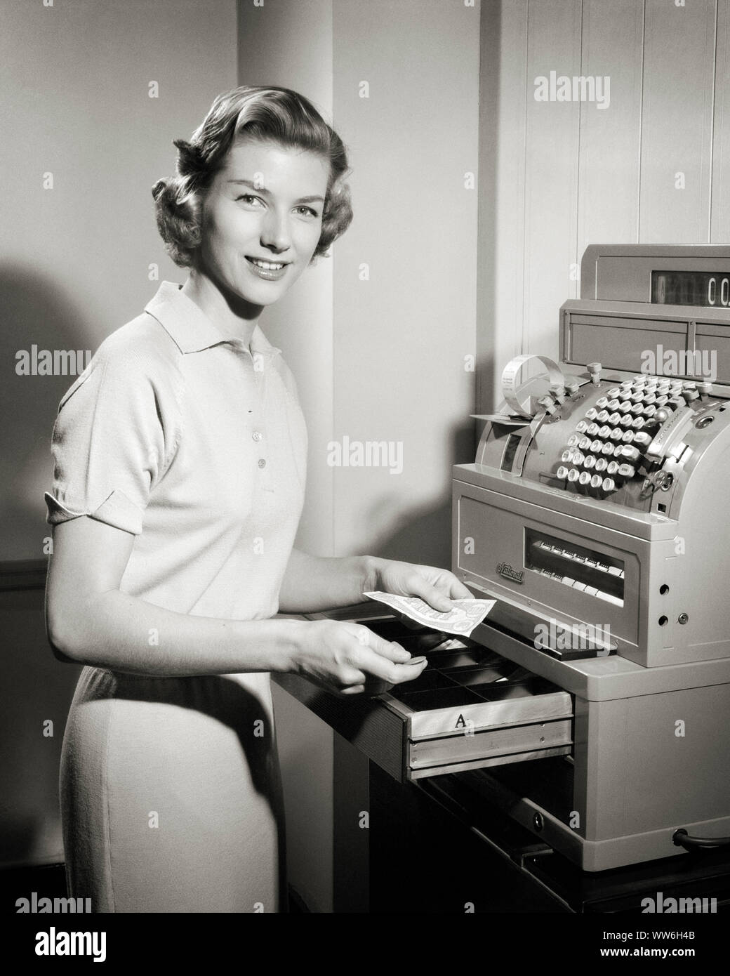 1950s SMILING WOMAN RETAIL CASHIER STANDING AT OPEN MANUAL CASH REGISTER TILL DRAWER MAKING CHANGE LOOKING AT CAMERA - s6087 HAR001 HARS RETAIL CHANGE LADIES PERSONS CONFIDENCE EXPRESSIONS B&W DRAWER SHOPPER SHOPPERS TILL SELLING MANUAL CUSTOMER SERVICE AT OCCUPATIONS CASHIERS SALESWOMAN SALESWOMEN STYLISH SALESCLERK YOUNG ADULT WOMAN BLACK AND WHITE CASH REGISTER CAUCASIAN ETHNICITY HAR001 OLD FASHIONED Stock Photo