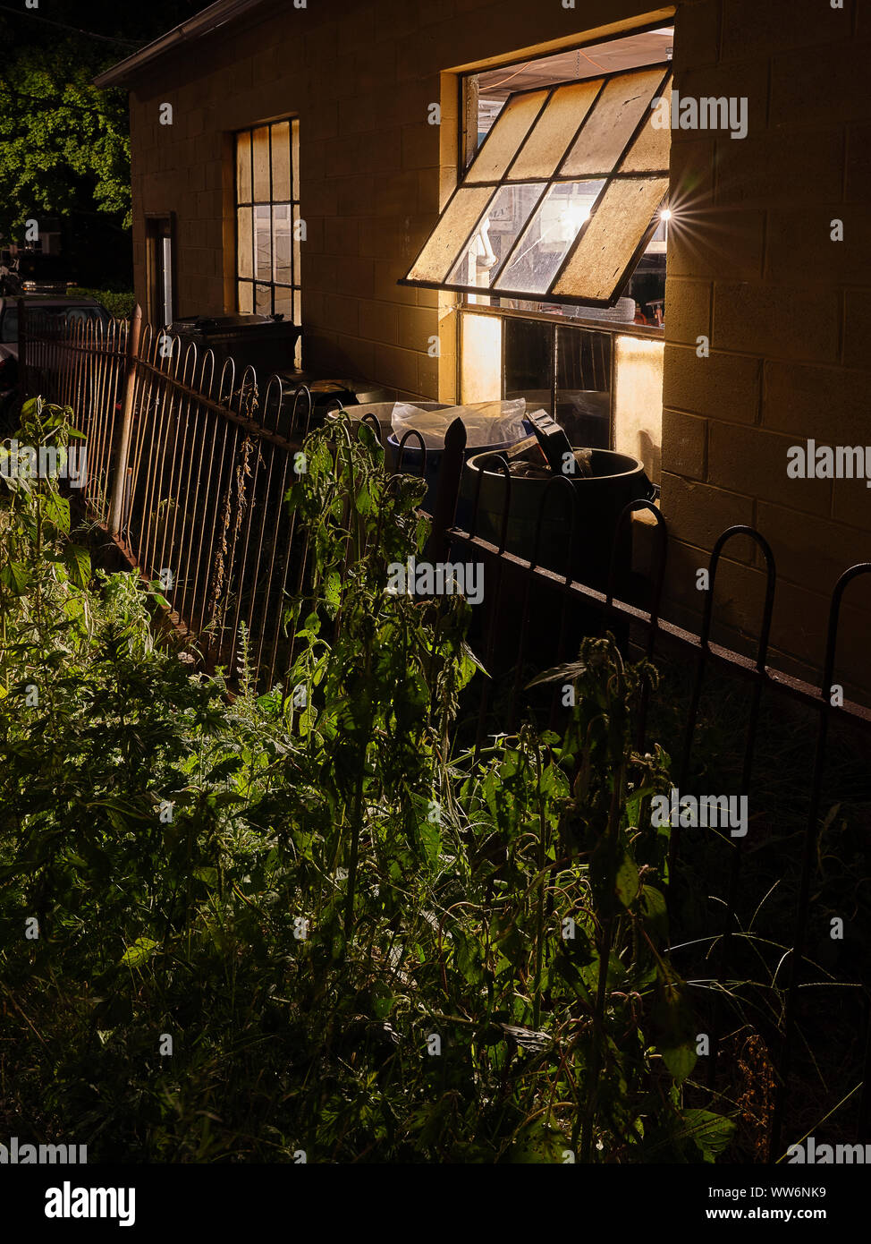 Open window with light and garbage trash cans at night Stock Photo