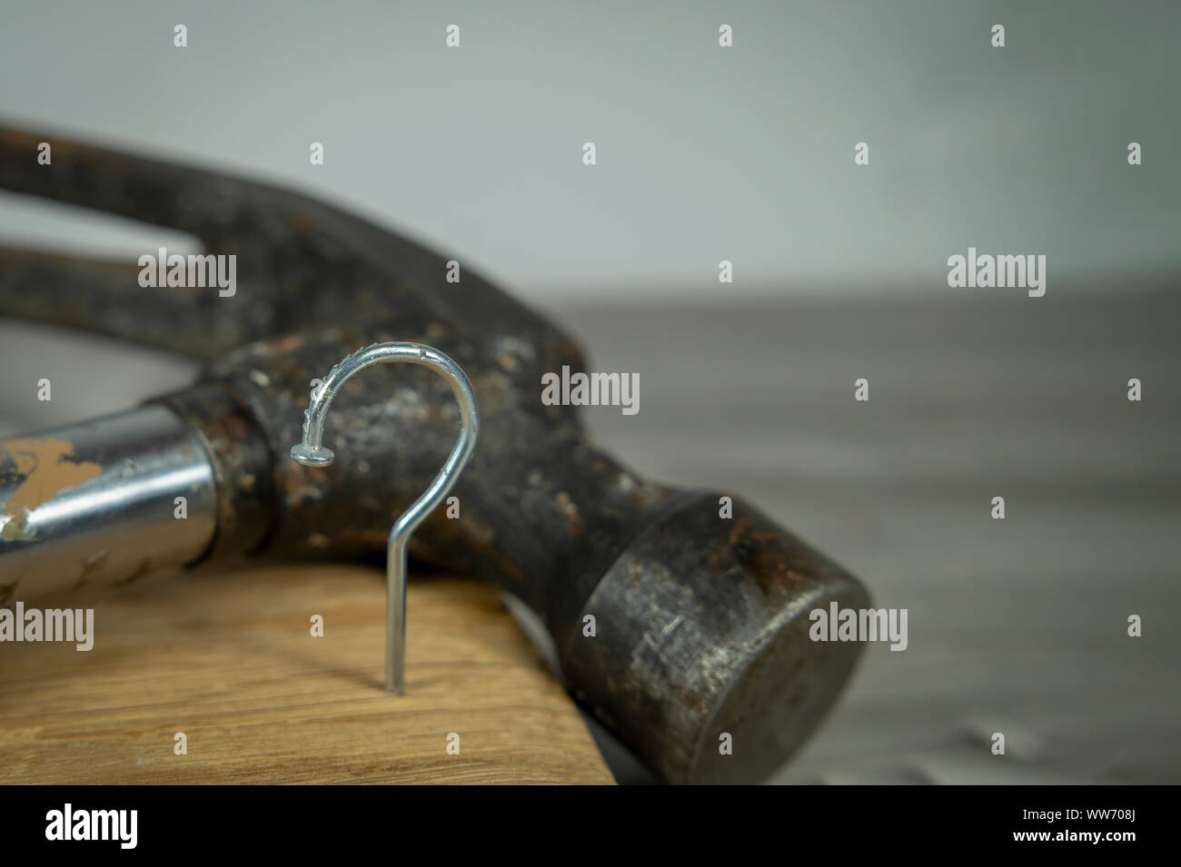 Construction nail shaped as question mark with blurred background of hammer, construction