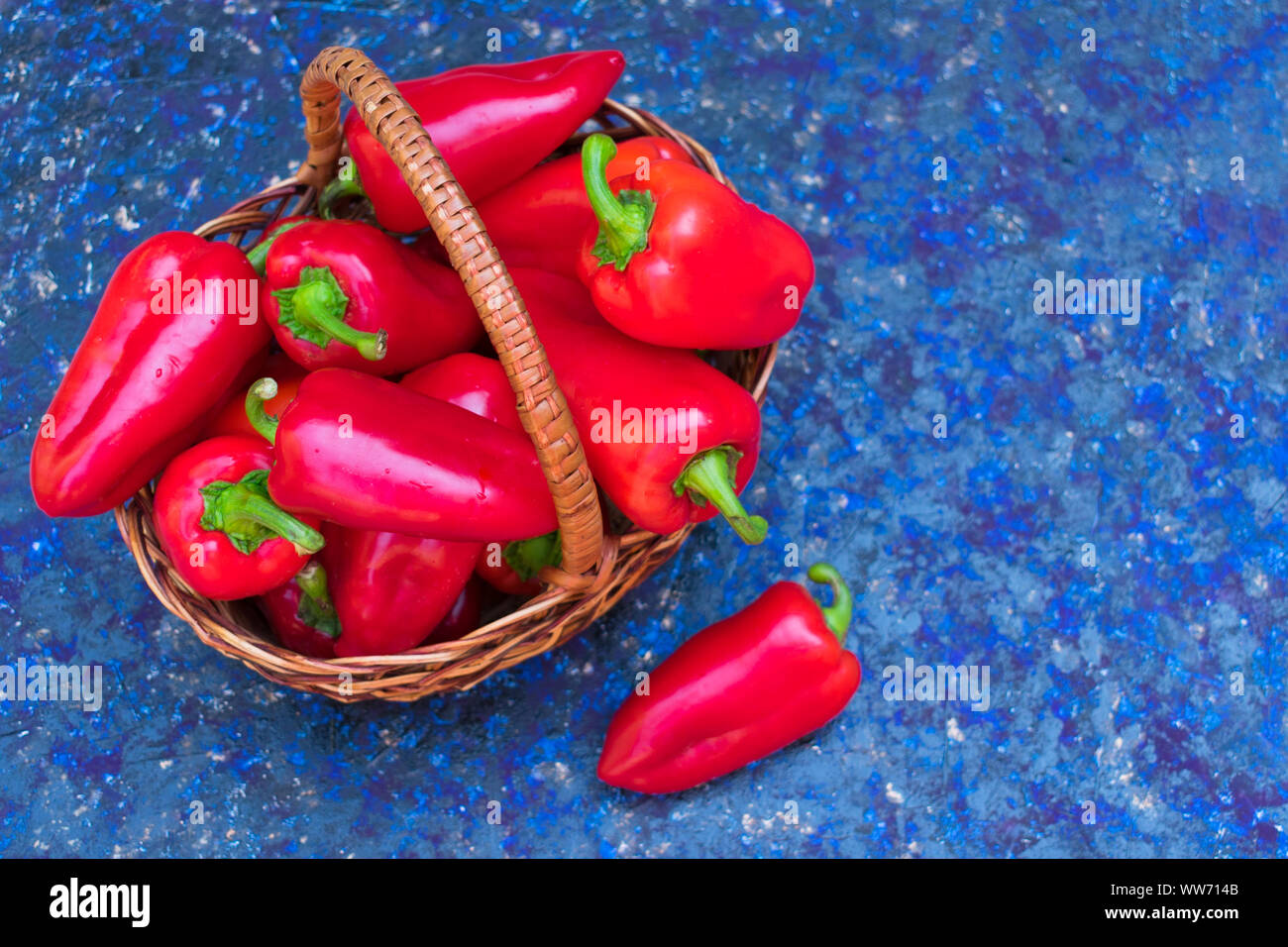 Red (sweet) bell peppers in a wicker basket on a blue background. Copy ...