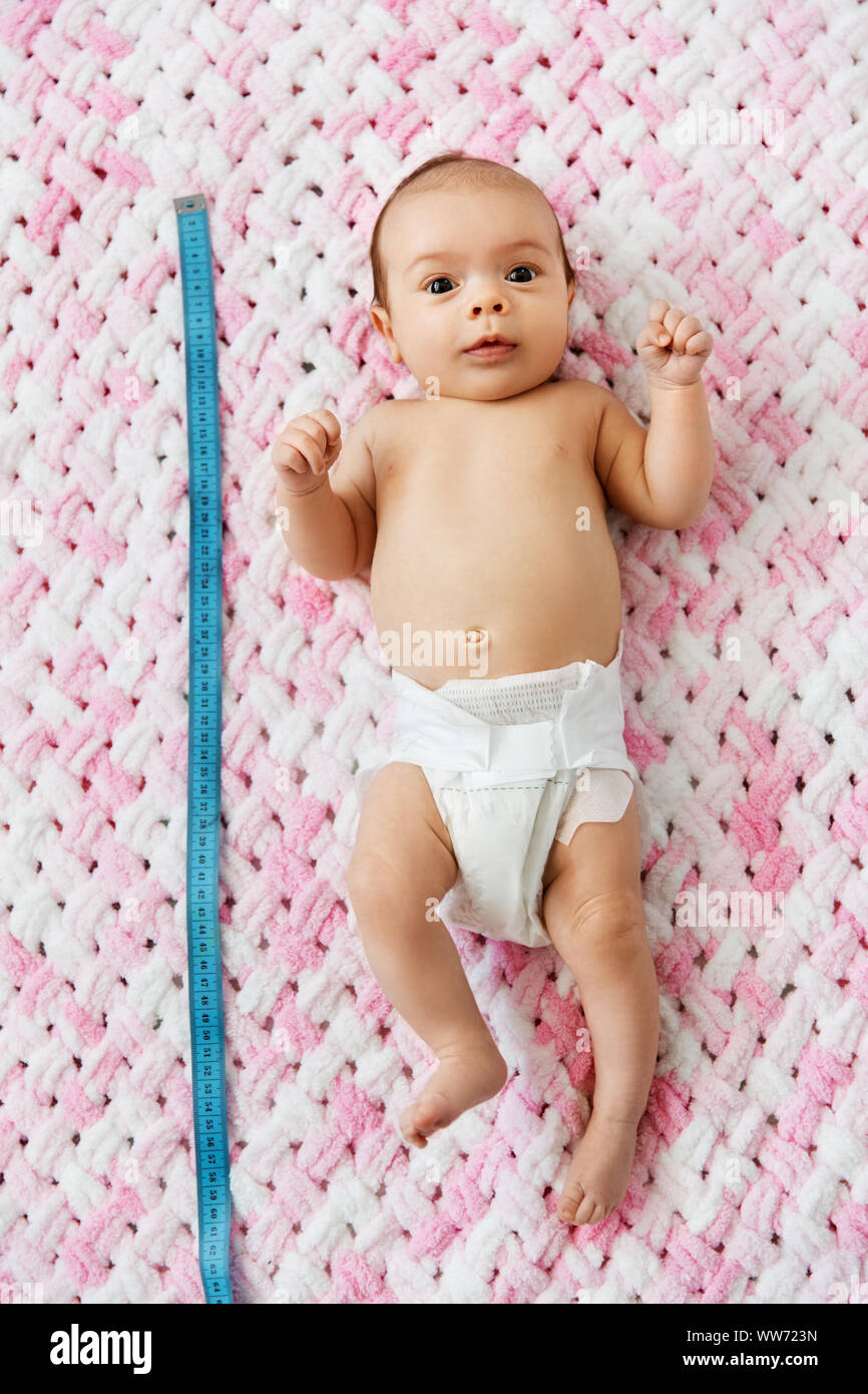baby girl lying with measure tape on blanket Stock Photo