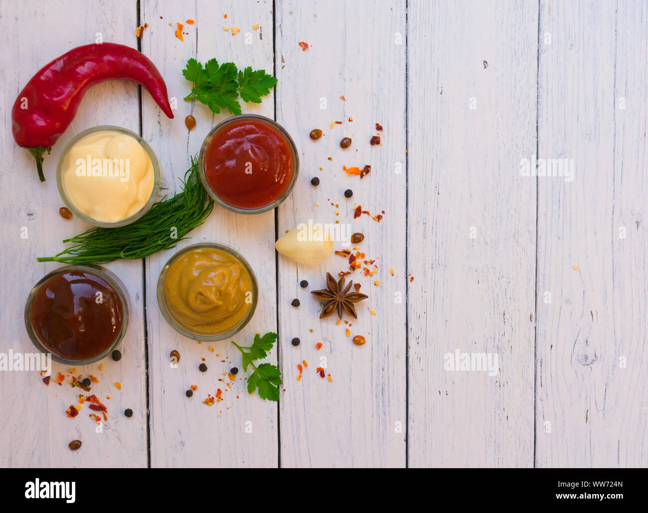 A set of sauces and a special one - ketchup, mayonnaise and mustard on a white plate, hot pepper, parsley, dill. Top view on white wooden background. Stock Photo