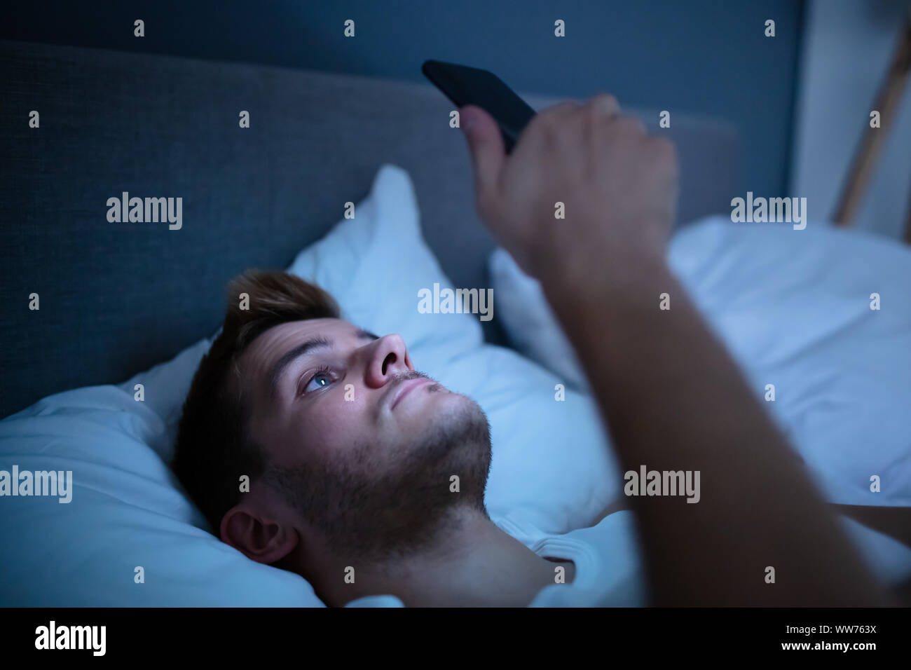 Man In Bed With Mobile Phone At Night Stock Photo
