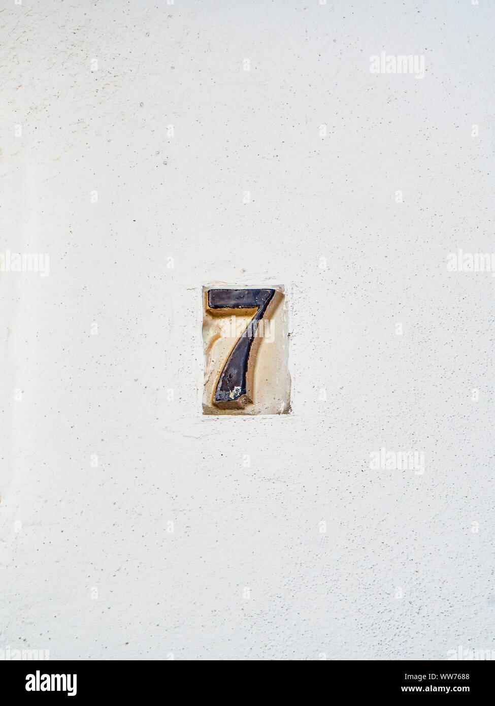 Antique ceramic tile number 7 on a whitewashed wall. Antique european style. Stock Photo