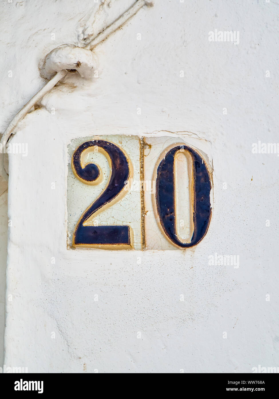 Antique ceramic tile number 20 on a whitewashed wall. Antique european style. Stock Photo