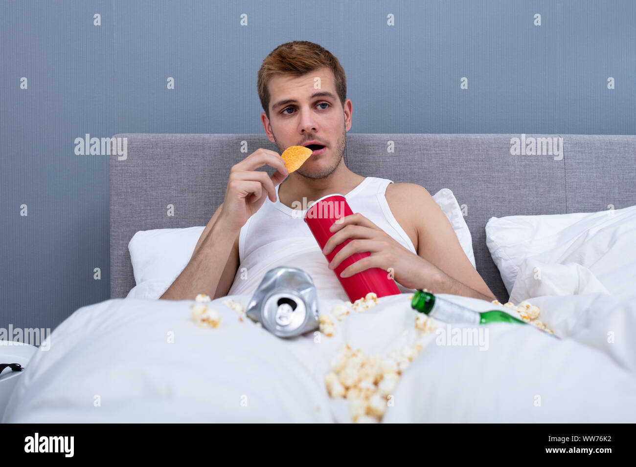 Man Eating In Messy Bed At Home Stock Photo