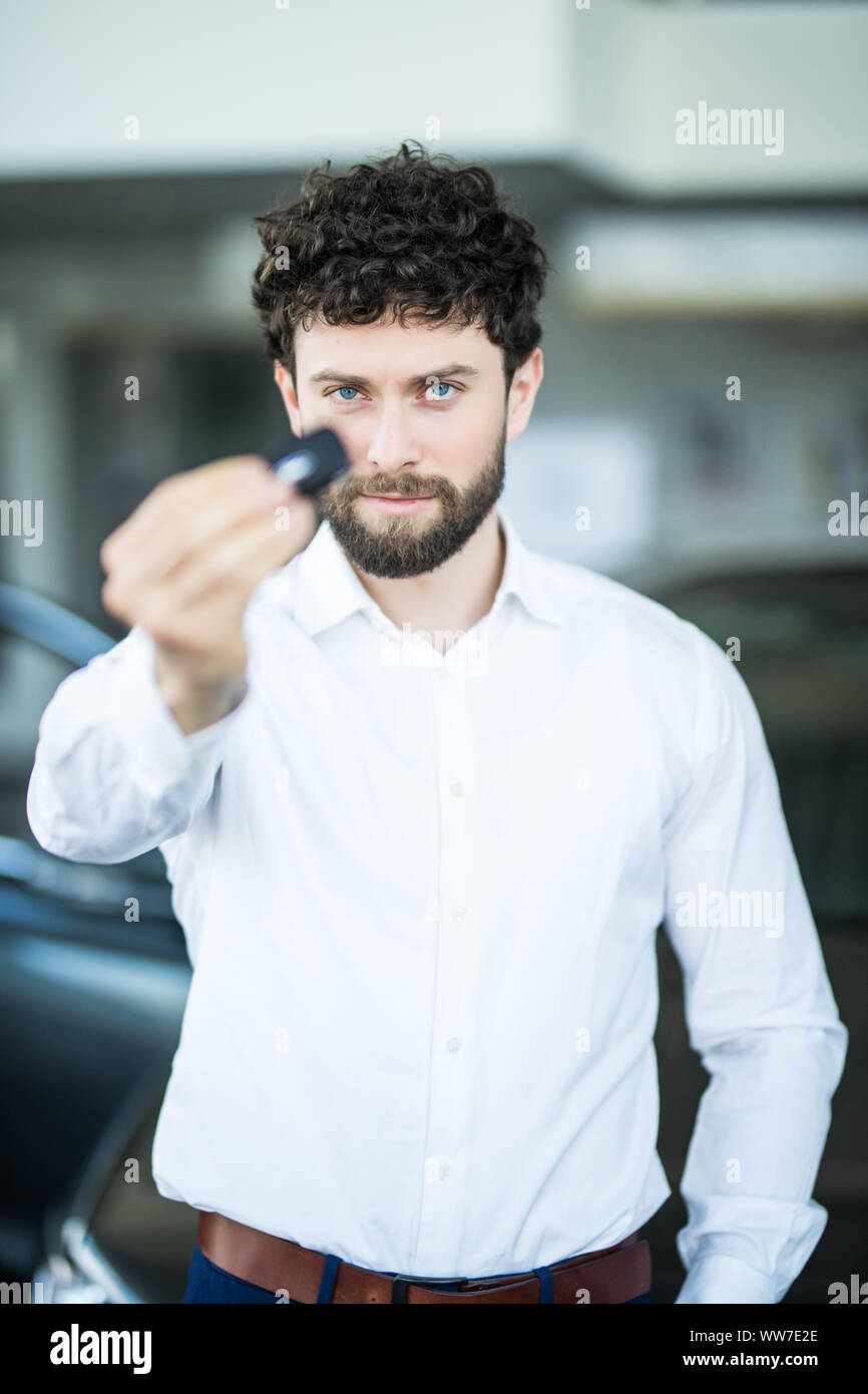 Car salesman in car dealership with key presenting his new and used