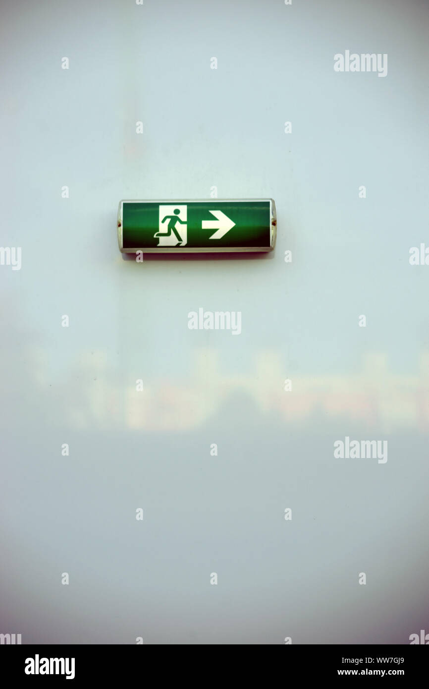 An illuminated green emergency exit sign bolted to a sheet metal wall, Stock Photo