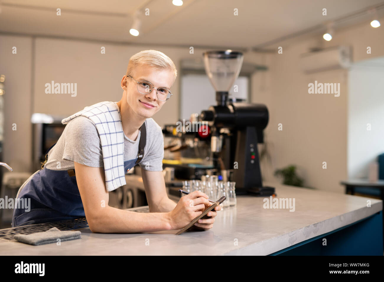 Young confident waiter with notepad and pen reading notes before preparing order Stock Photo