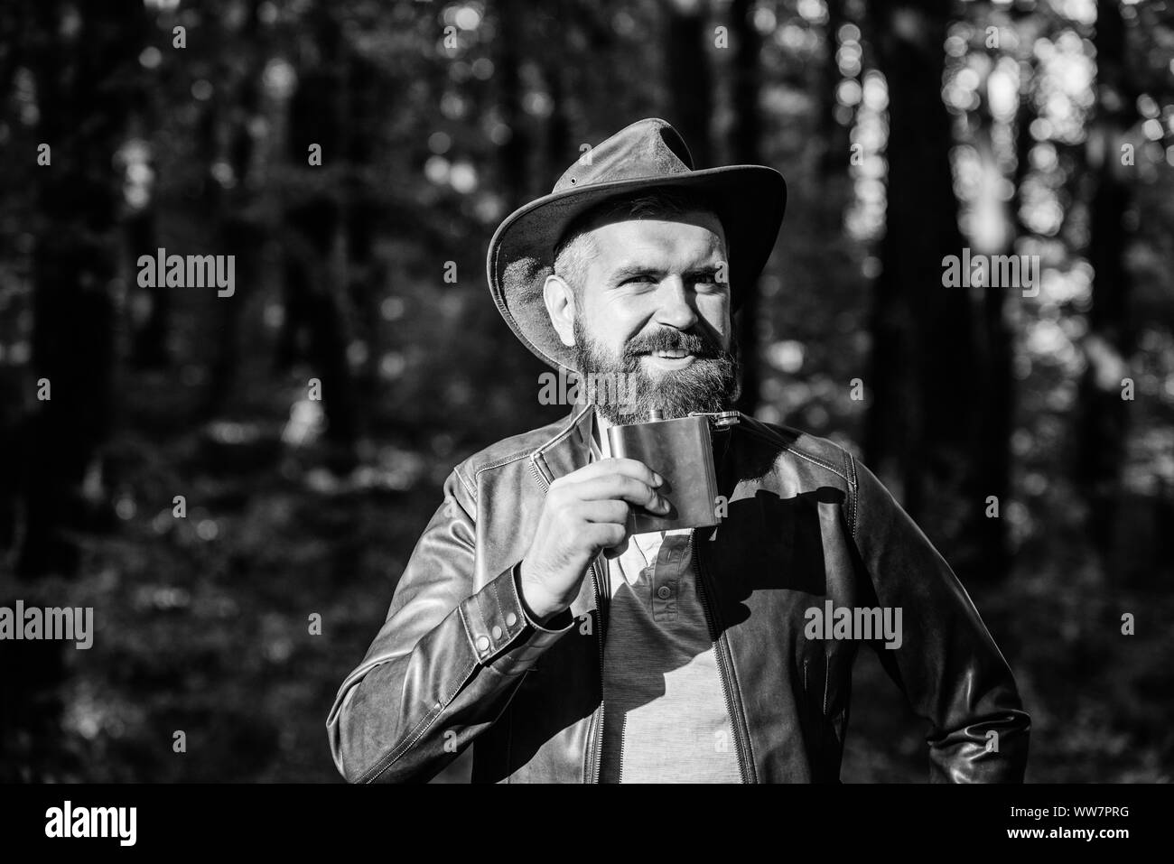 man hipster relax in autumn forest. Spring sunny weather. camping and hiking. mature male with brutal look drink alcohol from metallic flask. Bearded man in cowboy hat in park outdoor. Smiling cowboy. Stock Photo