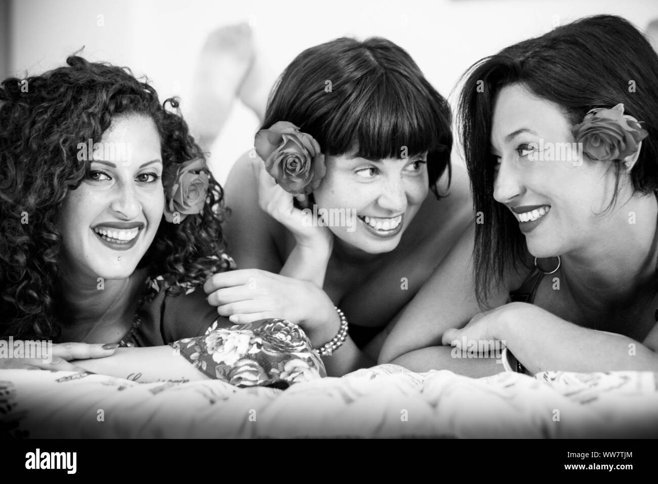 beautiful young women friends at home lay down on the bed with a rose in the hair stay together with happiness and having fun. friendship concept for group of people Stock Photo