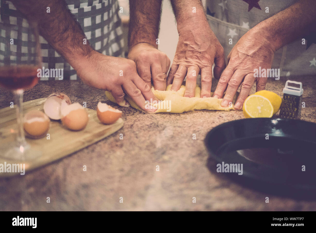 cake making of at home with two pair of men hands push the ingredients. eggs and lemon and wine, vintage brown warm filter and team concept Stock Photo