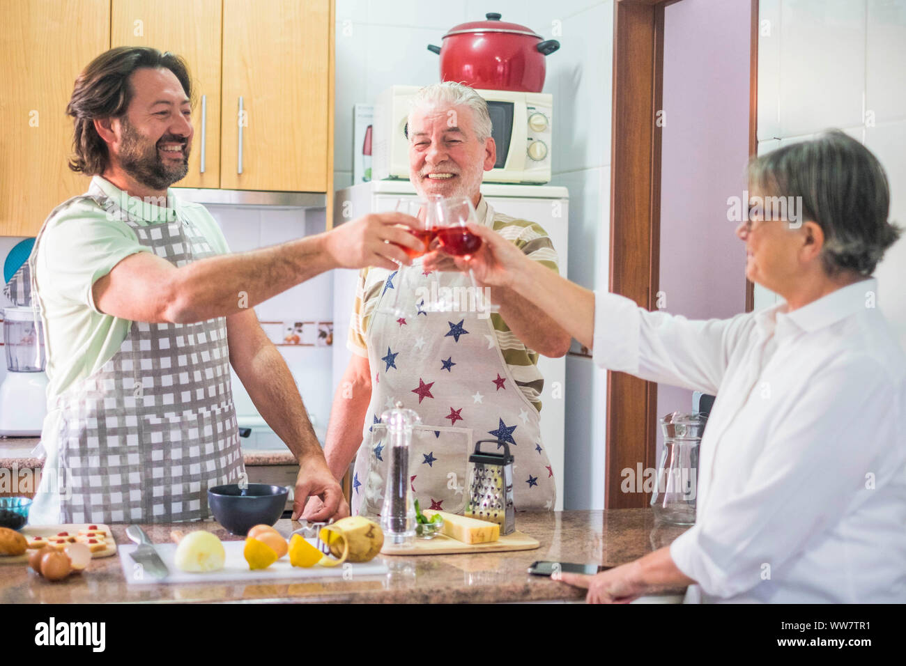 3-person family toasting with red wine while preparing dishes prepared in the home kitchen Stock Photo