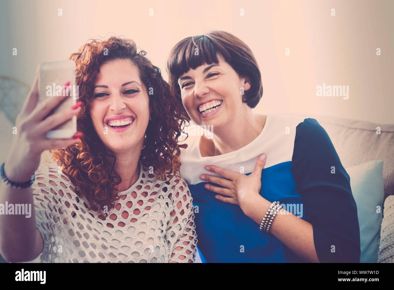 call friends with mobile phone in live video for a couple of beautiful middle age women at home. communicate and modern connected people concept. Stock Photo