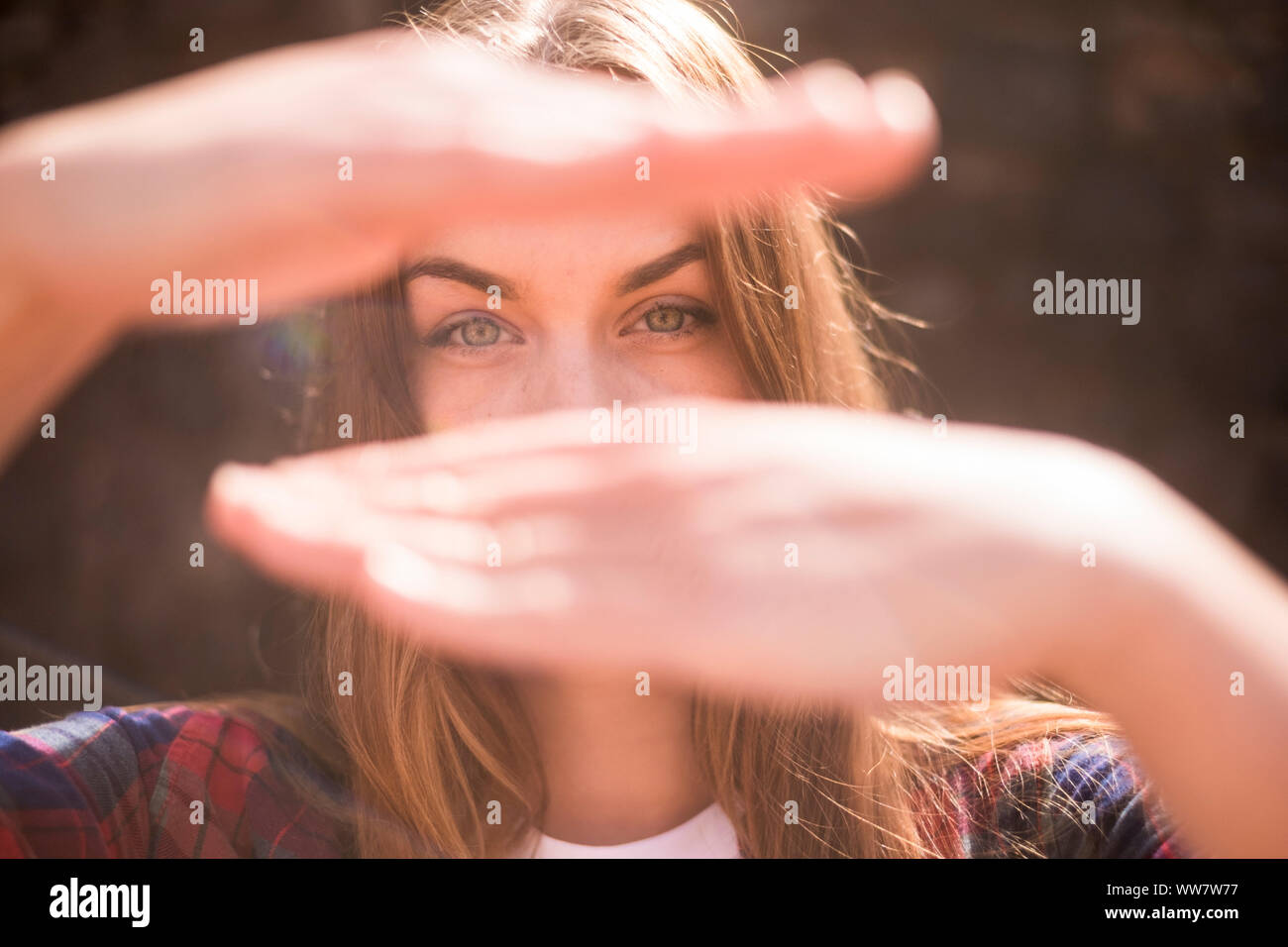 sunny portrait of beautiful model caucasian with blue eyes in backlight with hands in front of her face to hidden the mouth. bokeh defocused background Stock Photo