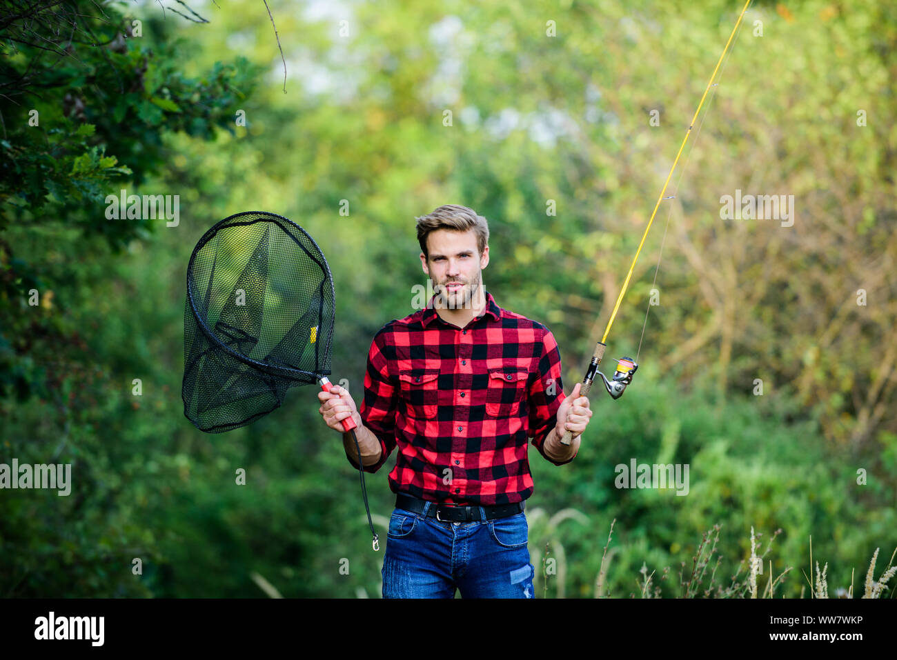 Fishing in my hobby. Handsome guy in checkered shirt with fishing equipment  nature background. Summer weekend concept. Hipster fisherman with rod  spinning net. Hope for nice fishing. Fishing day Stock Photo 